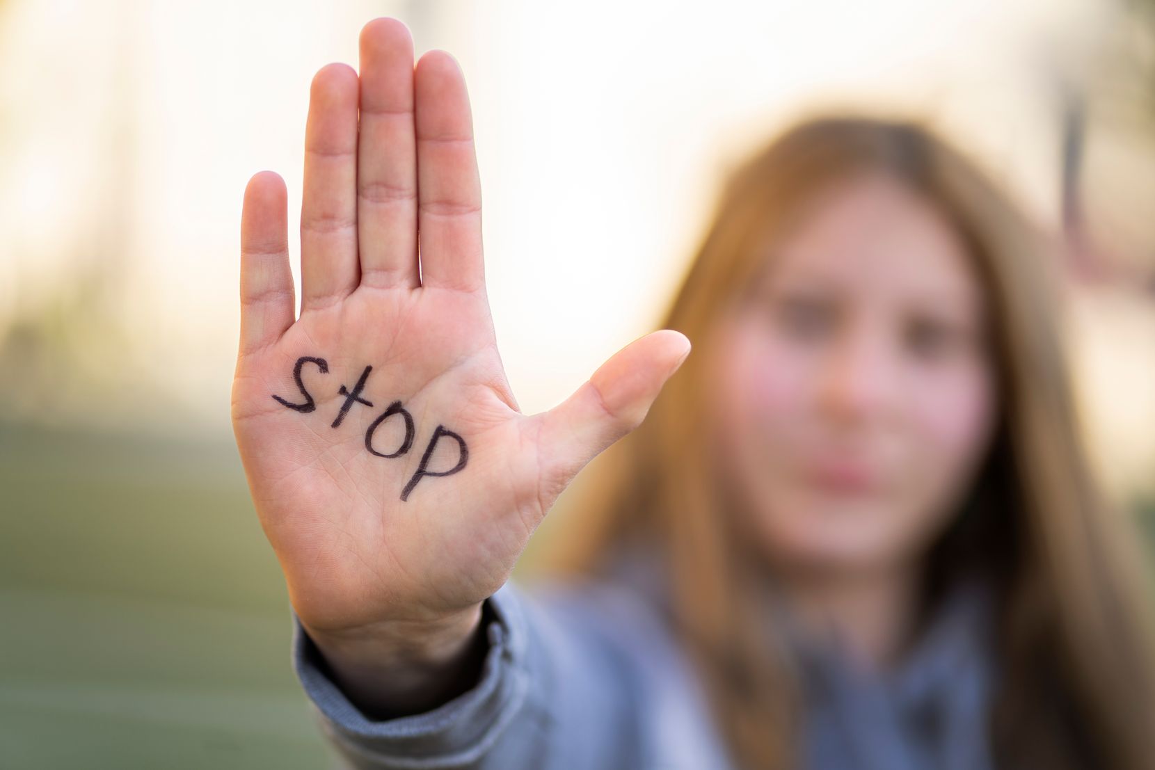 Man sieht eine Frau mit distanzierter Haltung, auf deren Hand «Stop» geschrieben steht.
